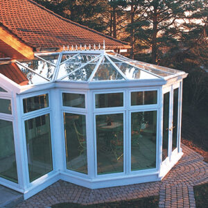 Image of a multi-sided solarium/sunroom off of a beautiful home with a cobblestone walking path alongside it